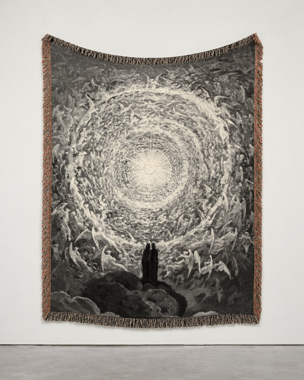 Paradiso woven blanket hung on a white gallery wall: a white rose of angels around a point of light, two small figures at its foot.