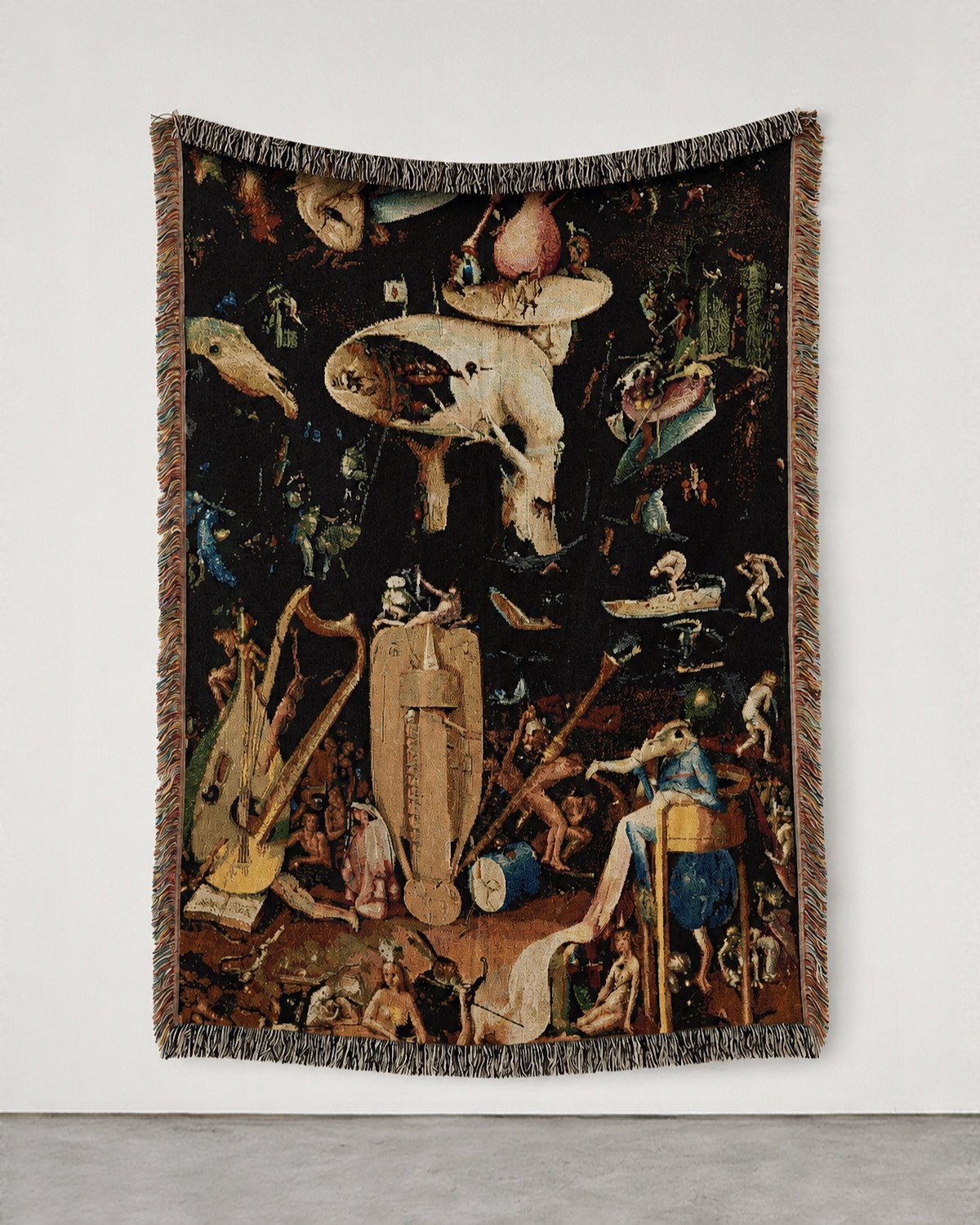 Hell woven blanket hung on a white gallery wall: Bosch's crowded panel with the tree-man and giant musical instruments.