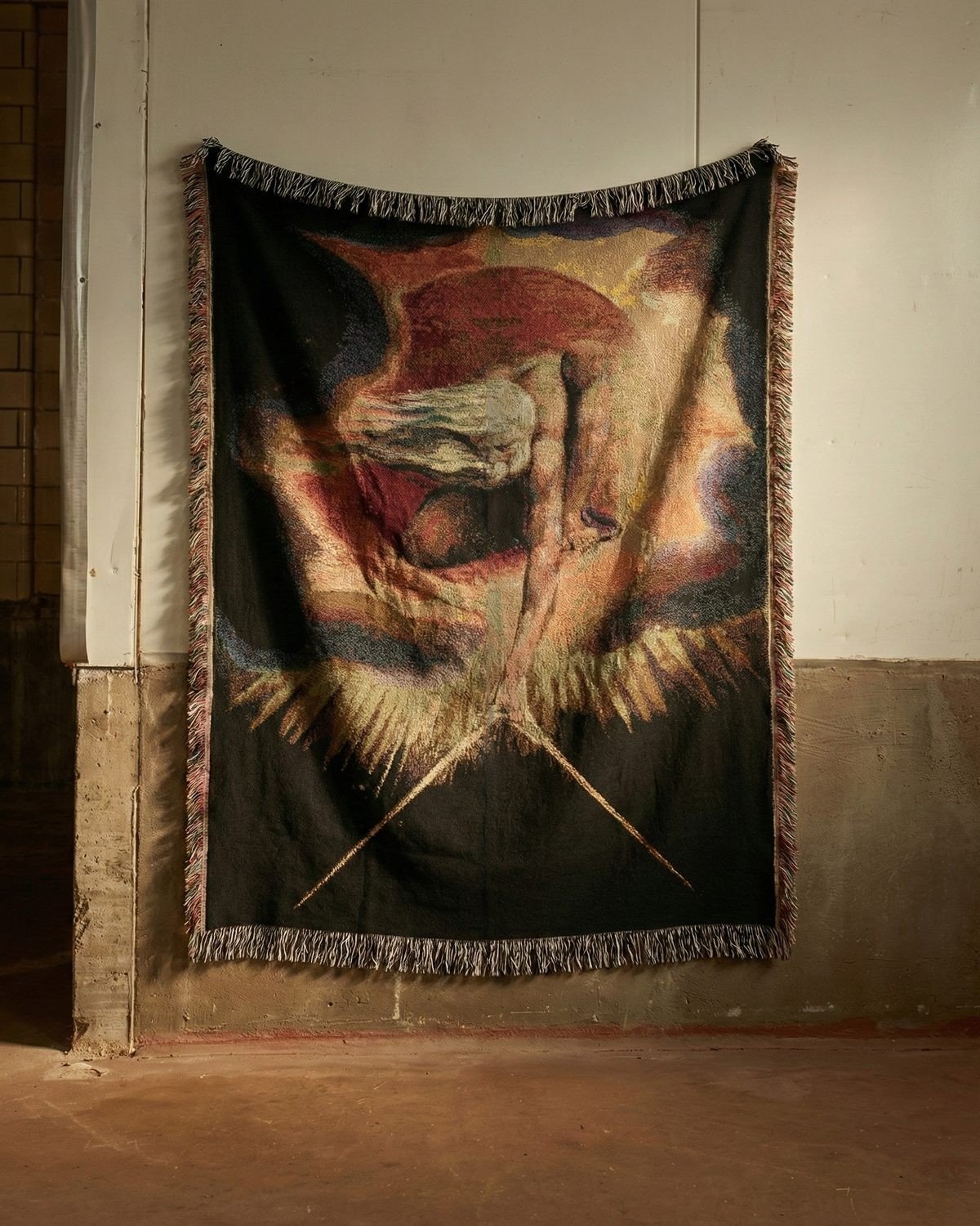 The Ancient of Days blanket hung on a whitewashed wall above a concrete base, in warm low light.